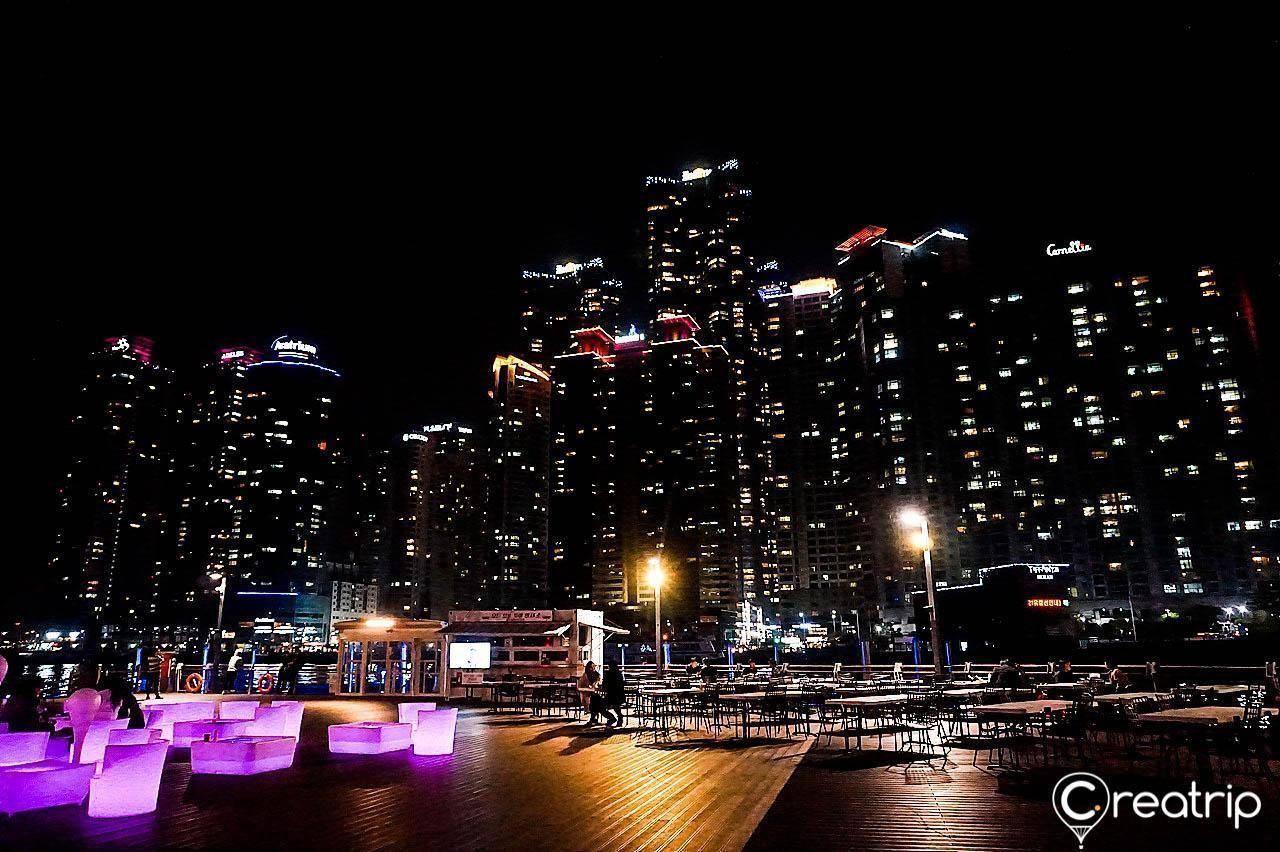 Night view of the Haeundae Bay area with skyscrapers and Gwangan Bridge in the background, capturing Busan's vibrant skyline.